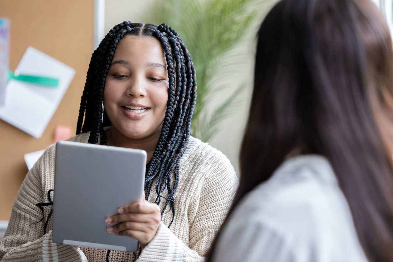 Aluno do ensino médio usando tablet digital se reúne com professor ou orientador.