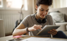 Jovem estudante sorridente usando tablet digital para estudar em casa.