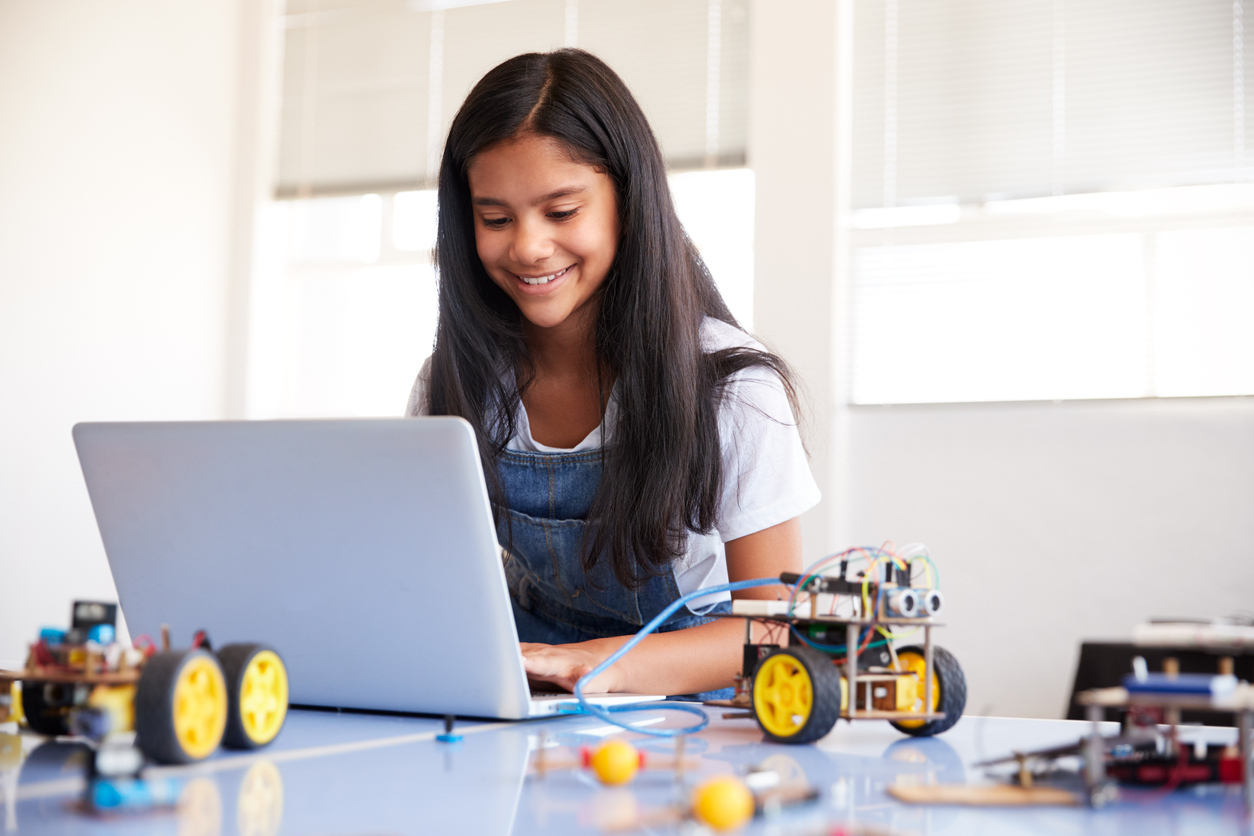 Aluna mexendo no notebook com itens de robótica na mesa.